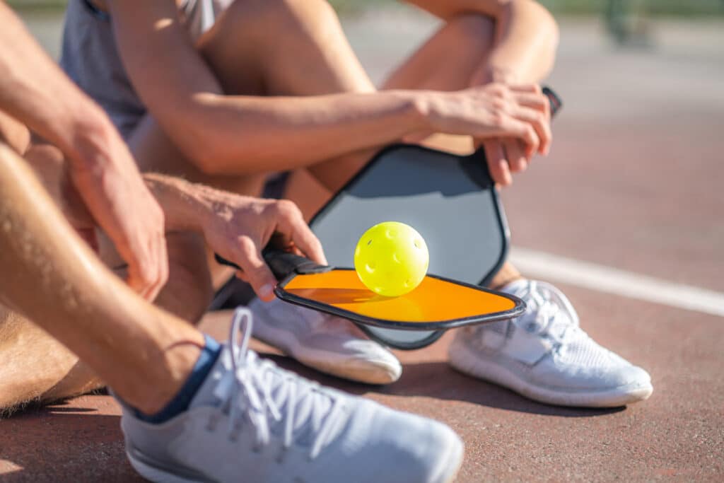 Pickleball paddle and ball resting on a player's knee on the court